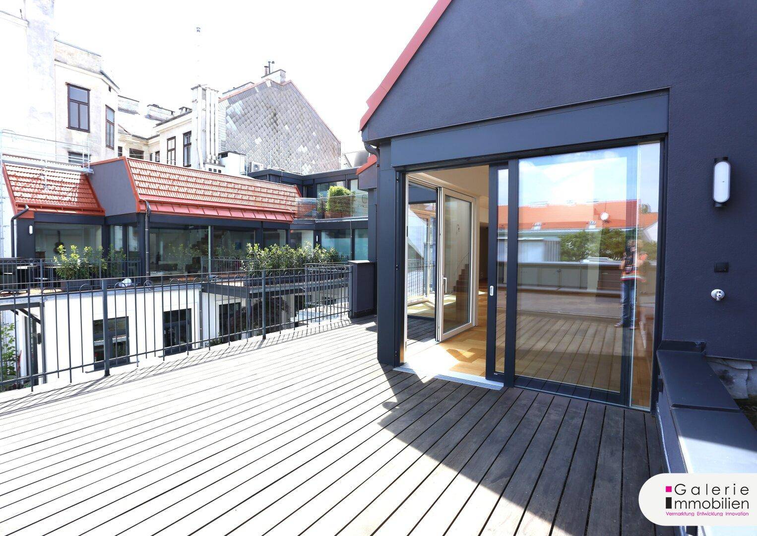 Sonniger Terrassenbereich mit Holzboden und großen Glasfronten, die den Innenraum mit dem Außenbereich verbinden.
