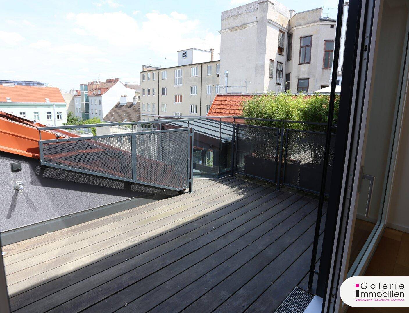 Blick von innen auf die Holzterrasse mit Metallgeländer und die umliegende Stadtlandschaft.