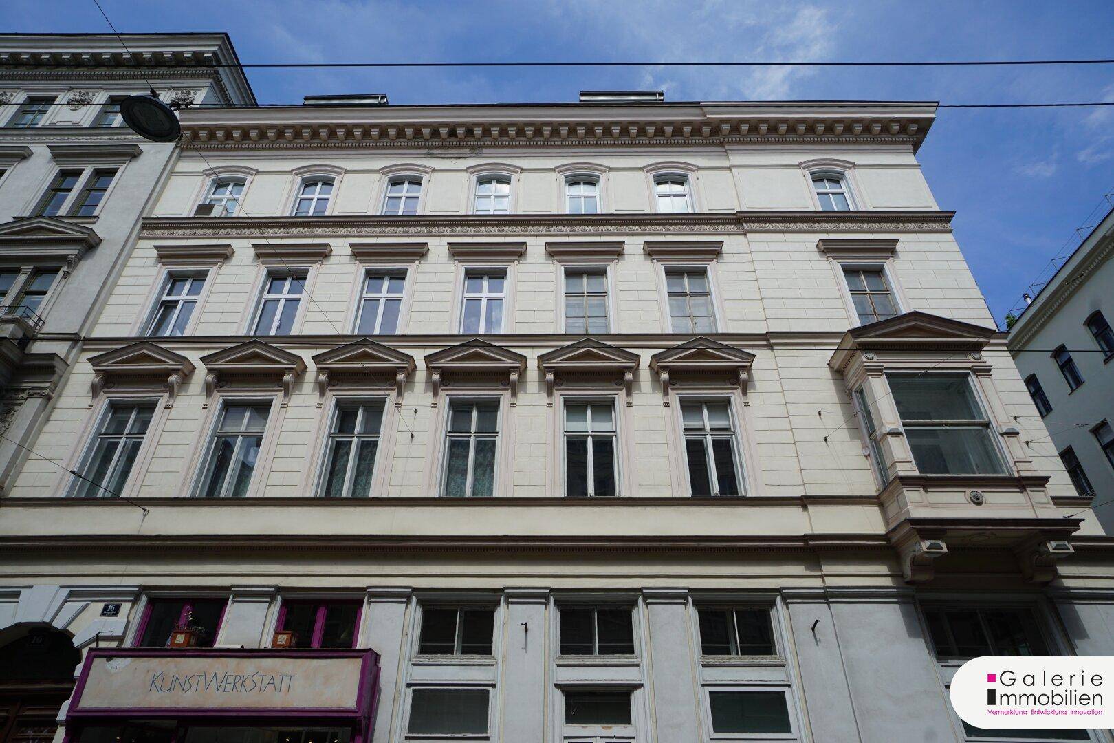 Klassische Fassade eines Altbaus mit vielen Fenstern und einem markanten Erker unter blauem Himmel.