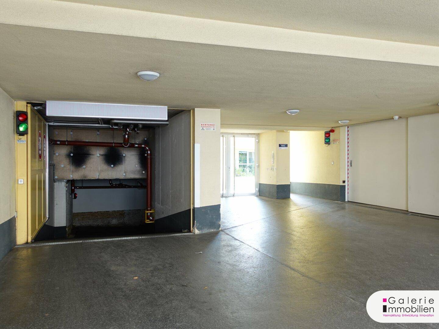 Offener Eingangsbereich einer Tiefgarage mit Rampe, sichtbaren Rohren und Verkehrsampeln.