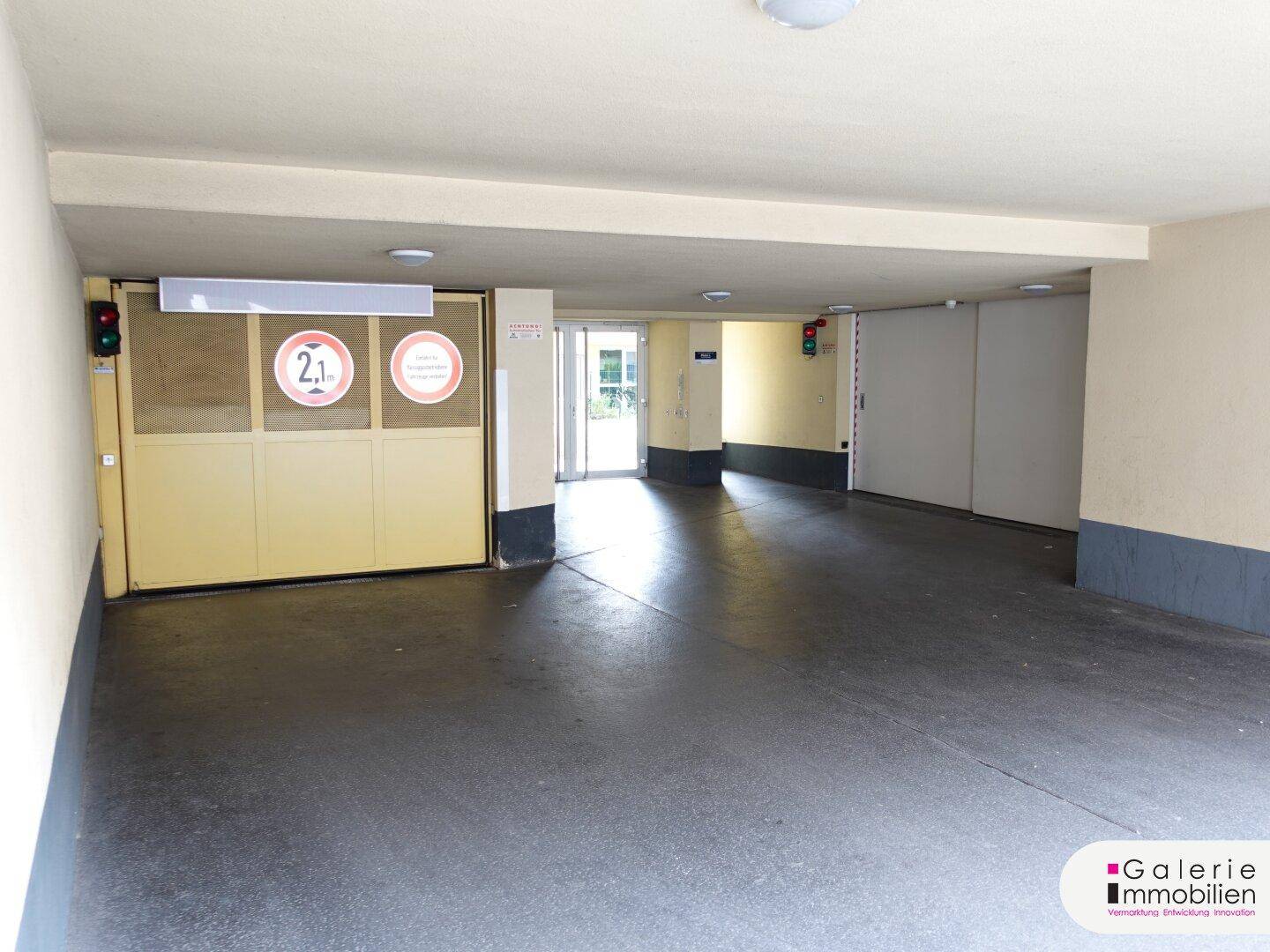 Eingangsbereich einer Tiefgarage mit dunklem Boden, gelbem Tor, Verkehrsampeln und Zugangstür.
