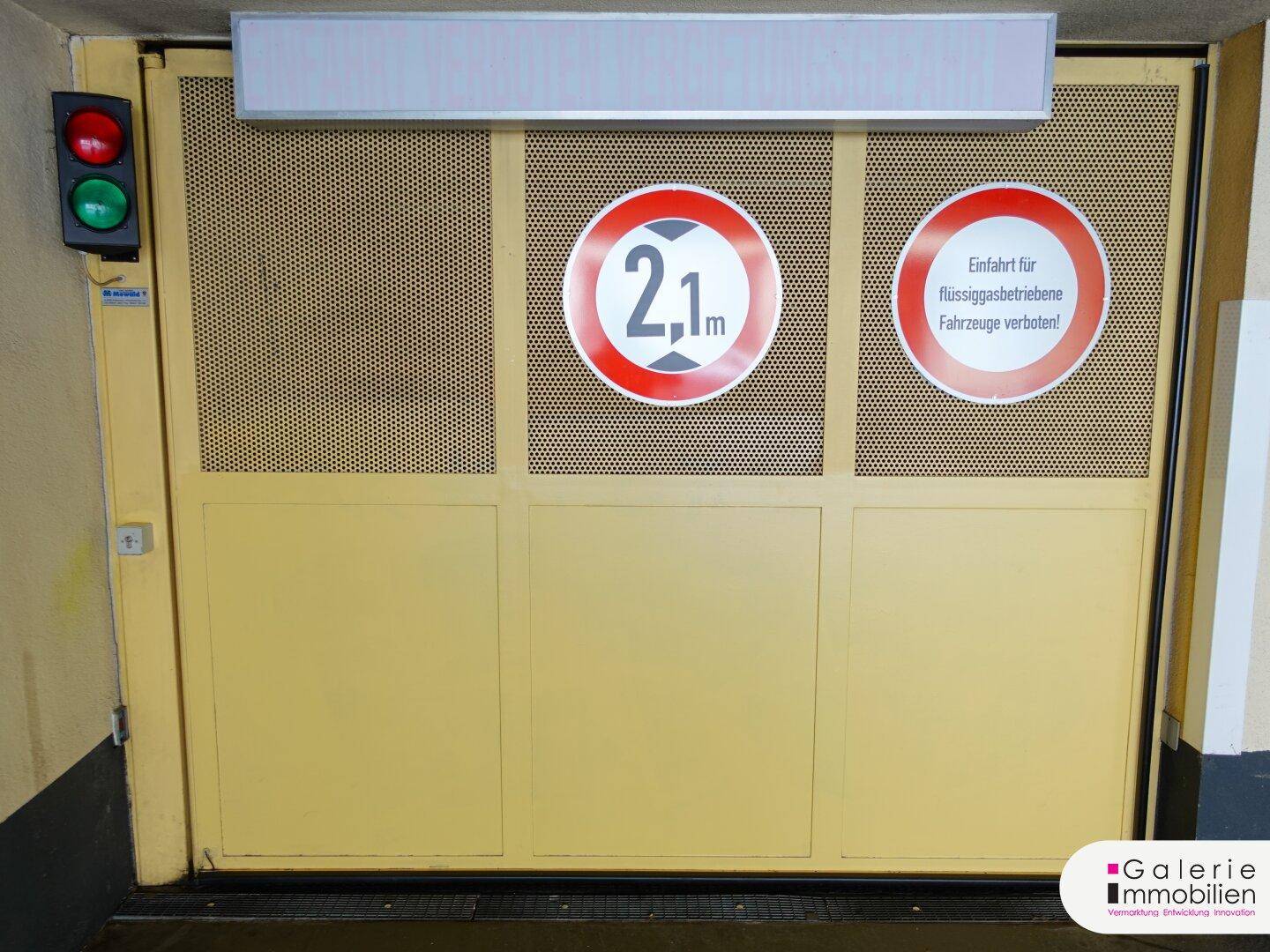 Nahaufnahme des gelben Tiefgaragentors mit Höhenbegrenzungsschildern und Verkehrsampel.