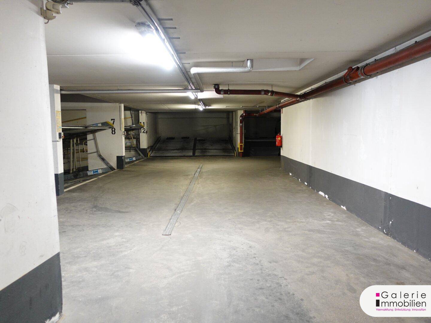 Tiefgarage mit Betonboden, weißen Wänden, sichtbaren Rohren und einem automatischen Parksystem.