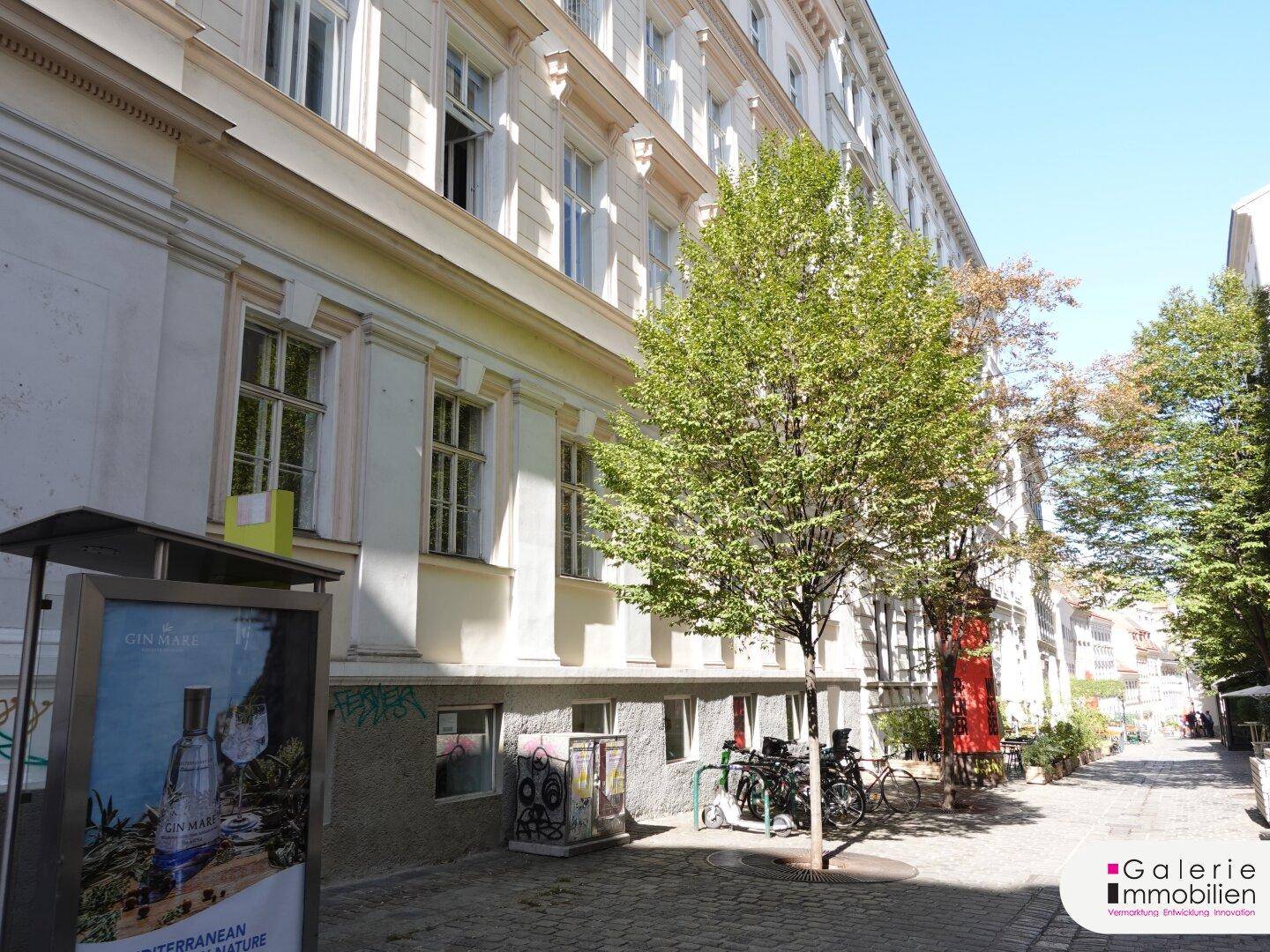 Die Fassade des Gebäudes zeigt klassische Architektur mit hohen Fenstern und einem Baum vor dem Eingangsbereich.