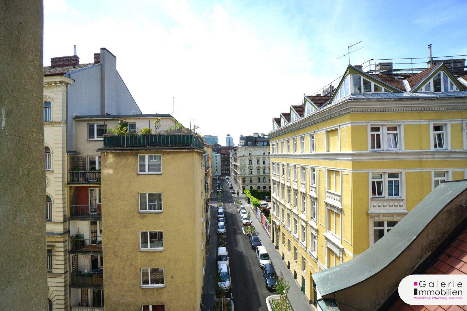 Blick aus dem Fenster auf eine belebte Stadtstraße mit historischen Gebäuden und parkenden Autos.