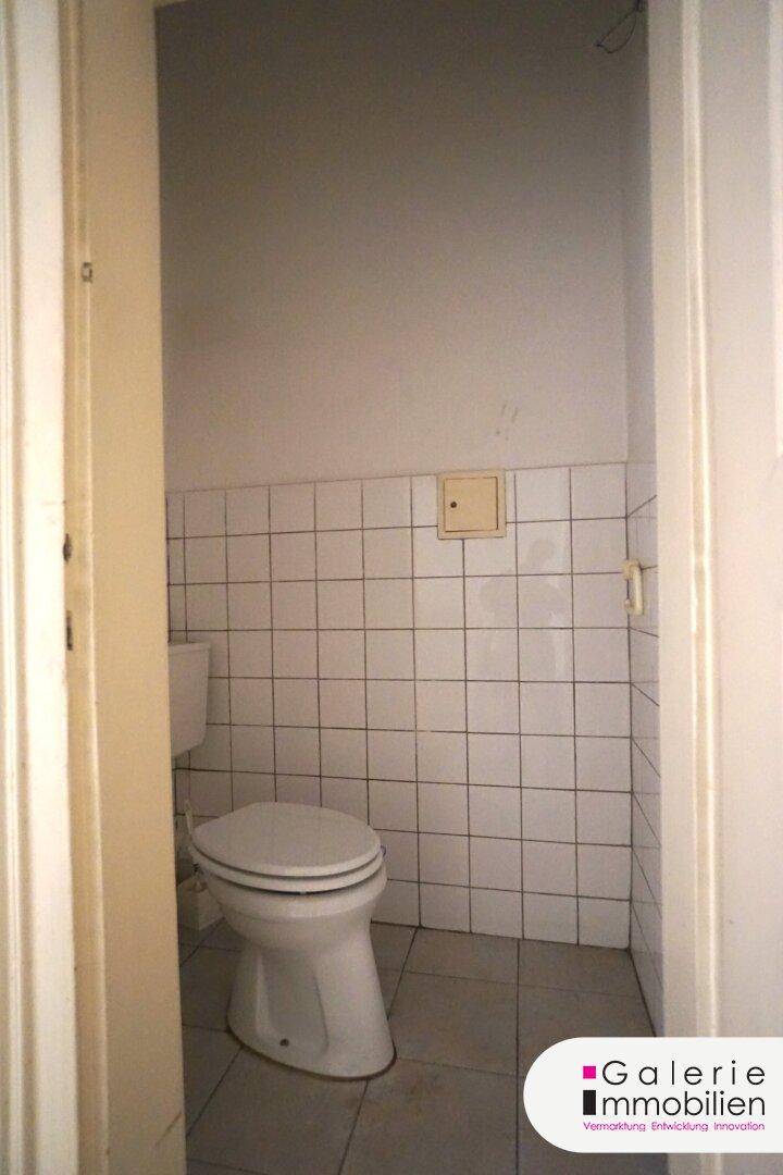 Separate Toilette mit weißen Fliesen an den Wänden und auf dem Boden.