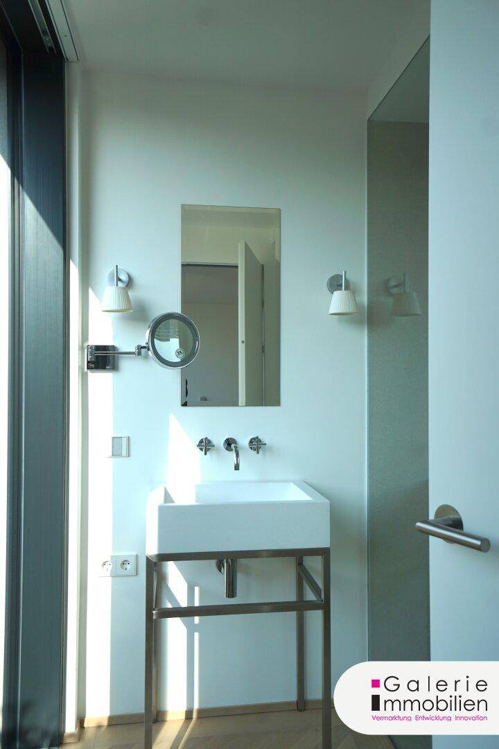 Detailansicht eines modernen Waschbeckens mit Spiegel und Wandleuchten im Badezimmer.