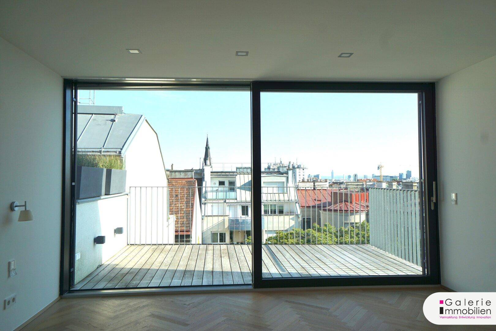 Heller Raum mit großen Schiebetüren, die zu einer Holzterrasse mit Stadtblick führen.