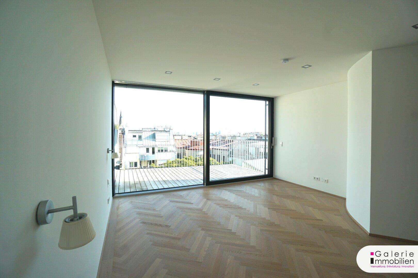 Lichtdurchfluteter Raum mit breiten Fensterfronten und Zugang zu einer Terrasse mit Panoramablick.