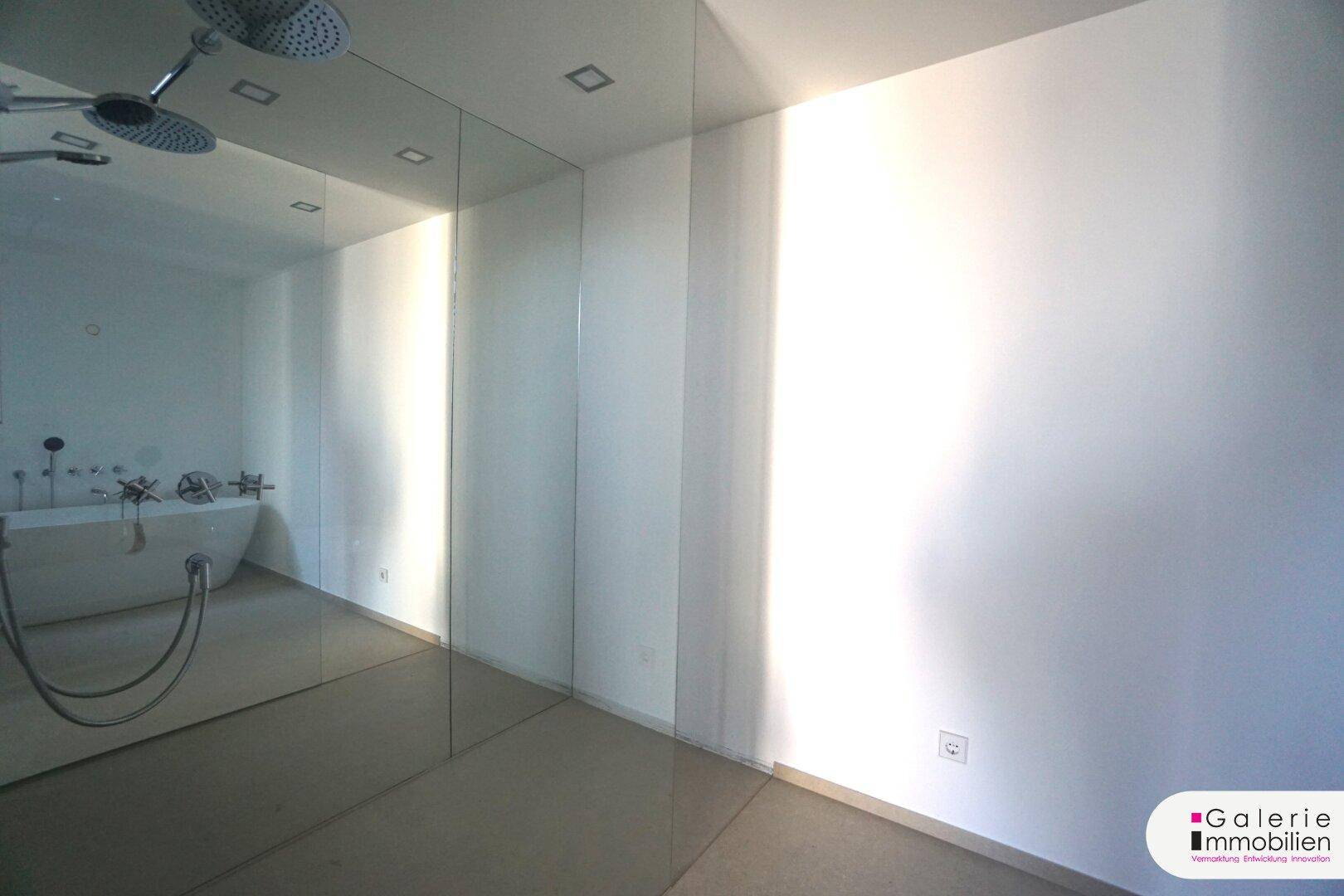Heller Badezimmerbereich mit großer Spiegelfläche und Reflexion einer freistehenden Badewanne.