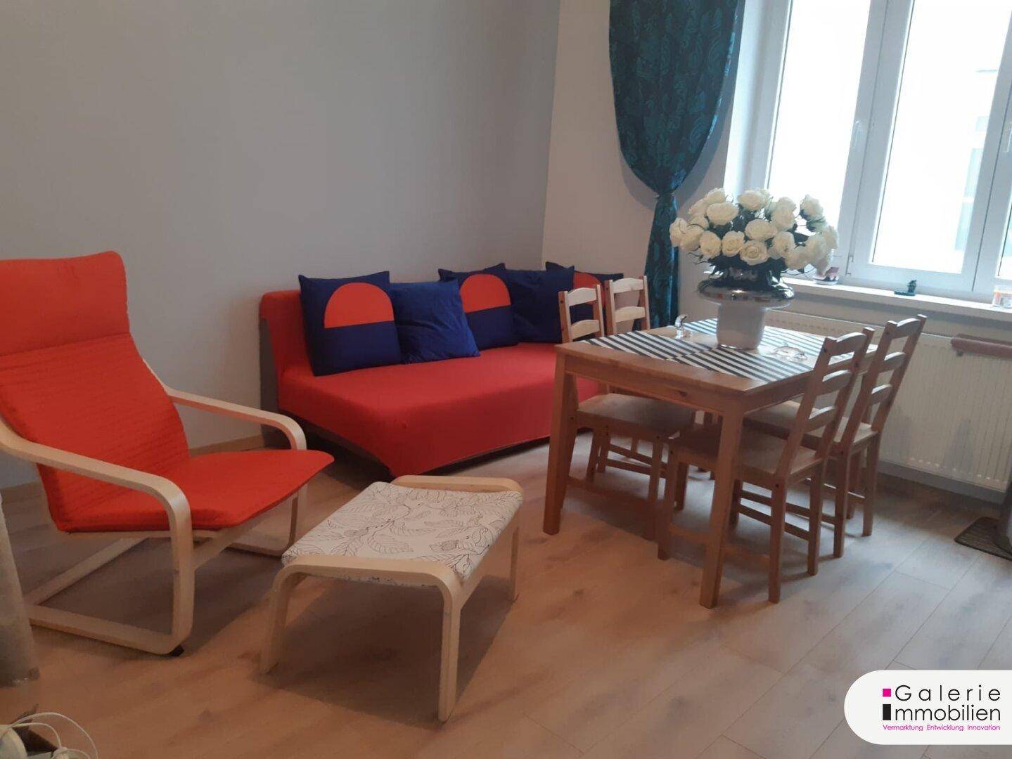 Heller Wohn- und Essbereich mit rotem Sofa, Holztisch und Laminatboden.
