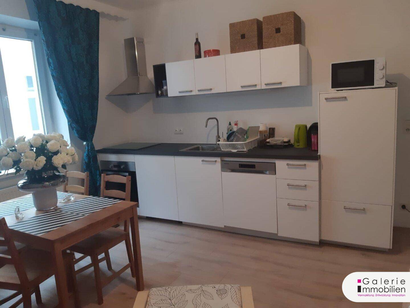 Moderne Küche mit weißen Schränken, integrierten Geräten und Essbereich.