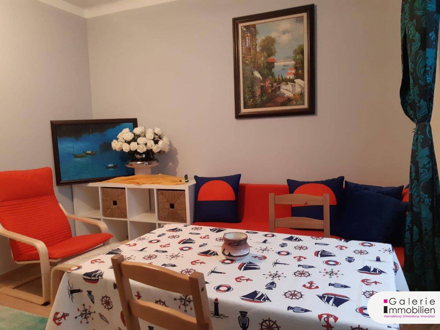 Detailansicht des Wohn-Essbereichs mit rotem Sofa, Esstisch und dekorativen Bildern.