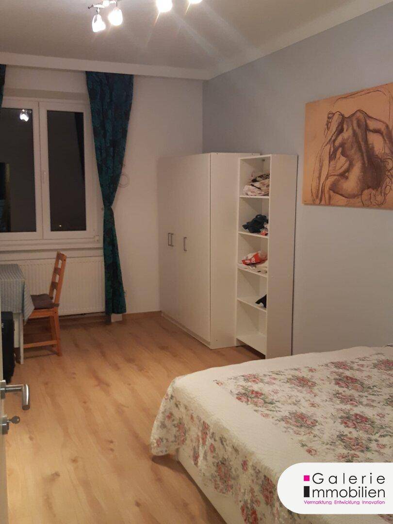 Helles Schlafzimmer mit Laminatboden, weißem Schrank und Blick zum Fenster.