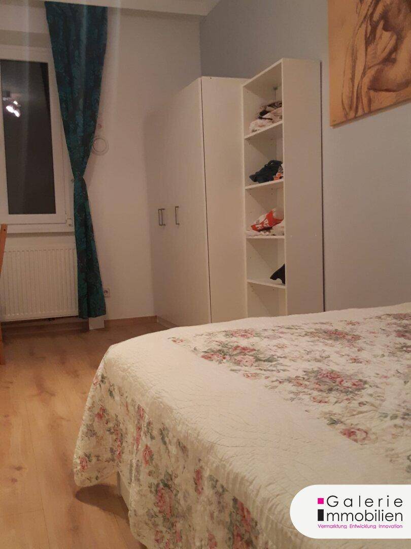 Schlafzimmer mit Doppelbett, weißem Kleiderschrank und Fenster.