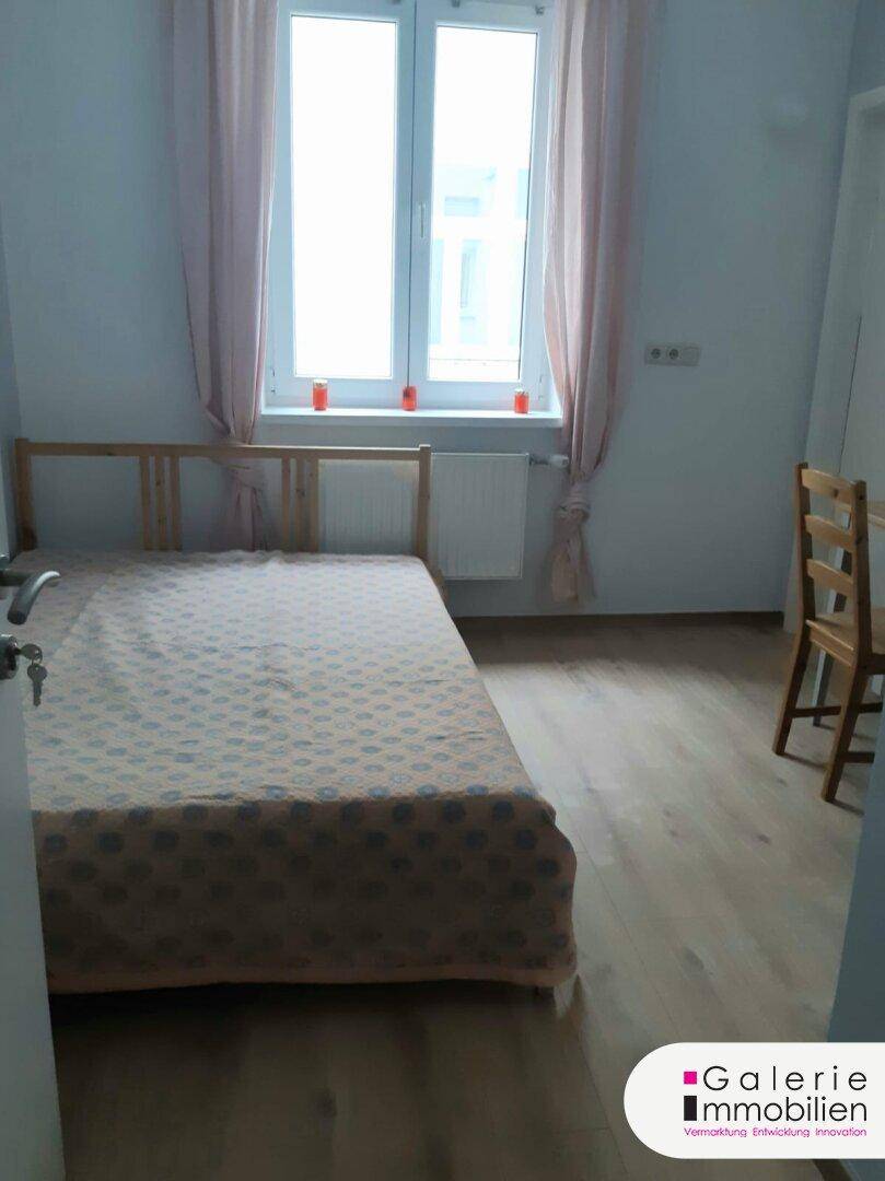 Schlafzimmer mit Einzelbett und großem Fenster, das viel Tageslicht hereinlässt.