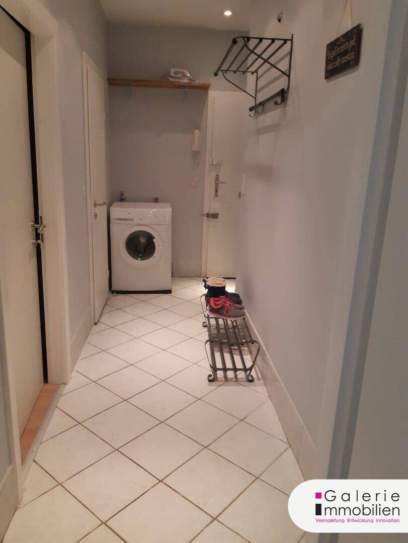 Flur mit Waschmaschine, Fliesenboden und Garderobe.