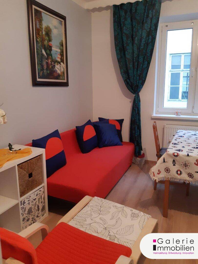 Gemütlicher Wohn-Essbereich mit rotem Sofa, Holztisch und Blick zum Fenster.