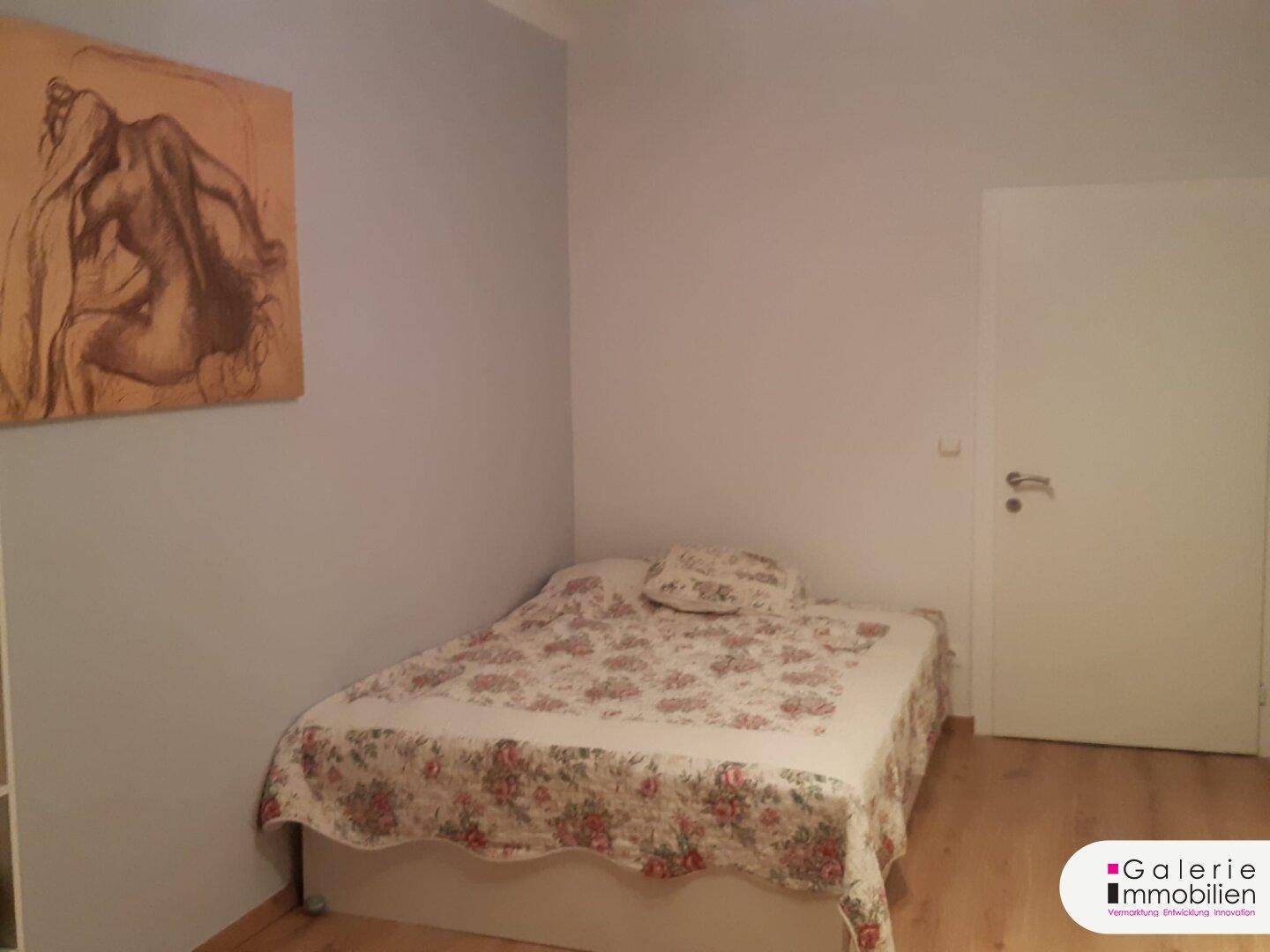 Schlafzimmer mit Bett, floraler Tagesdecke und Kunstwerk an der Wand.