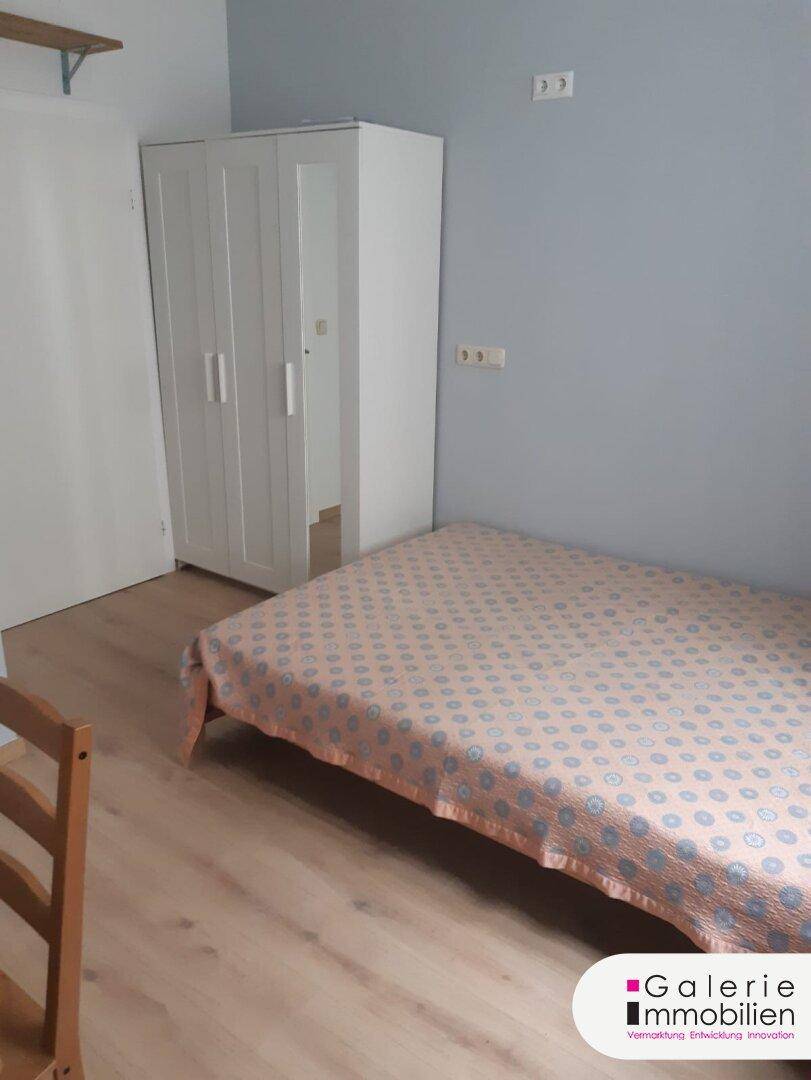 Schlafzimmer mit Bett, weißem Kleiderschrank und Laminatboden.