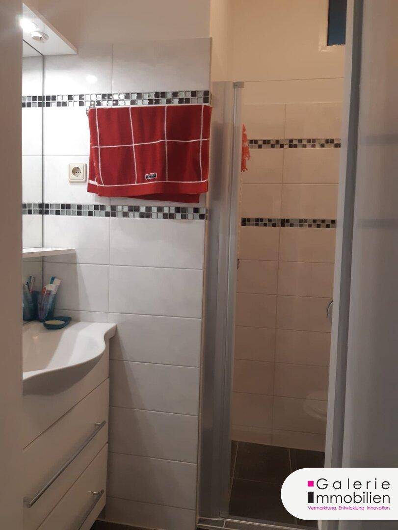 Helles Badezimmer mit Waschbecken, Spiegel und Duschbereich.