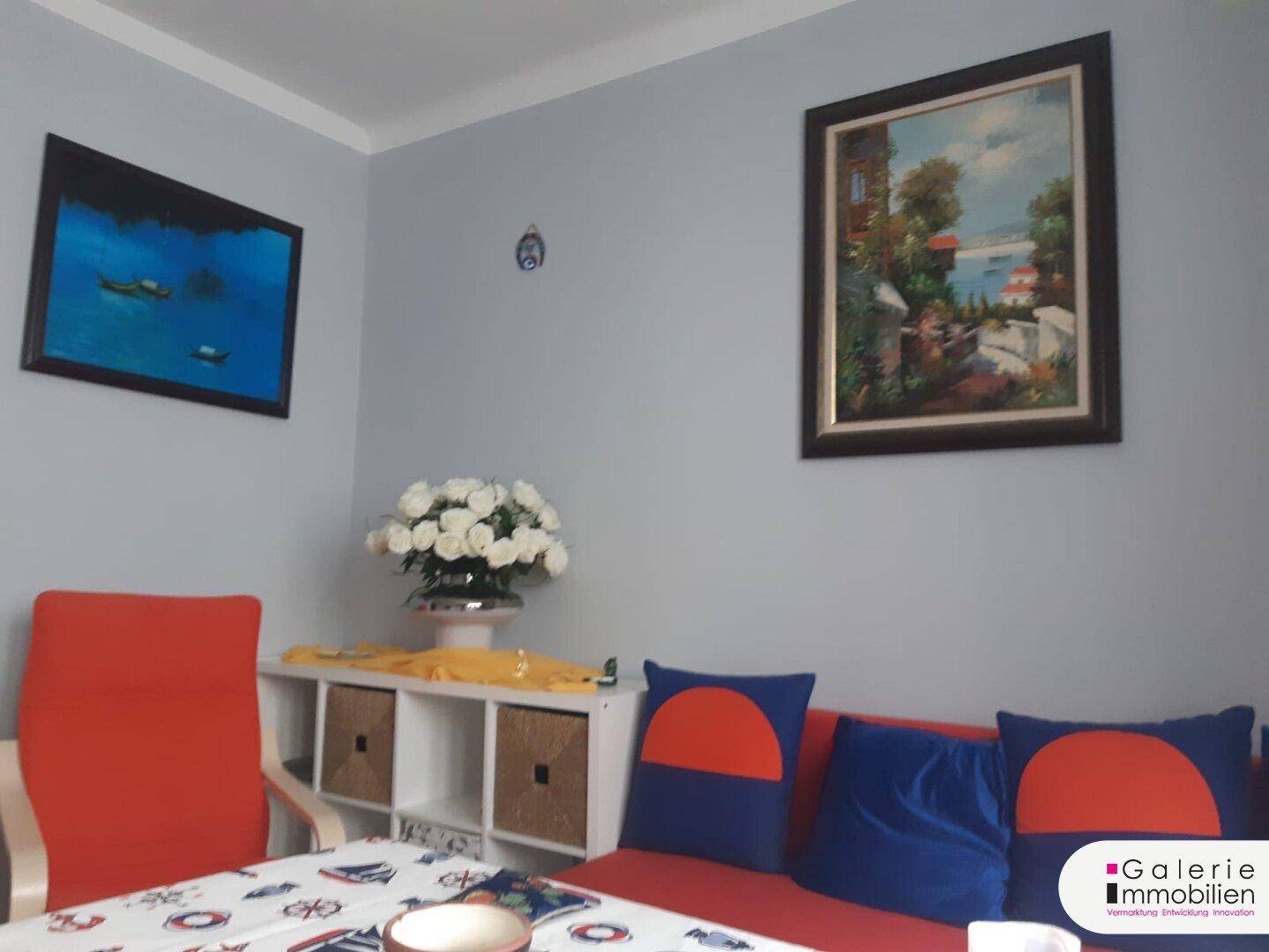 Wanddekoration und Sitzbereich im Wohn-Esszimmer mit rotem Sofa und weißen Rosen.