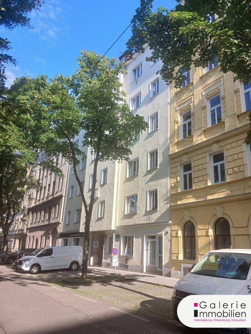 Fassade eines Mehrfamilienhauses an einer von Bäumen gesäumten Straße mit parkenden Autos.