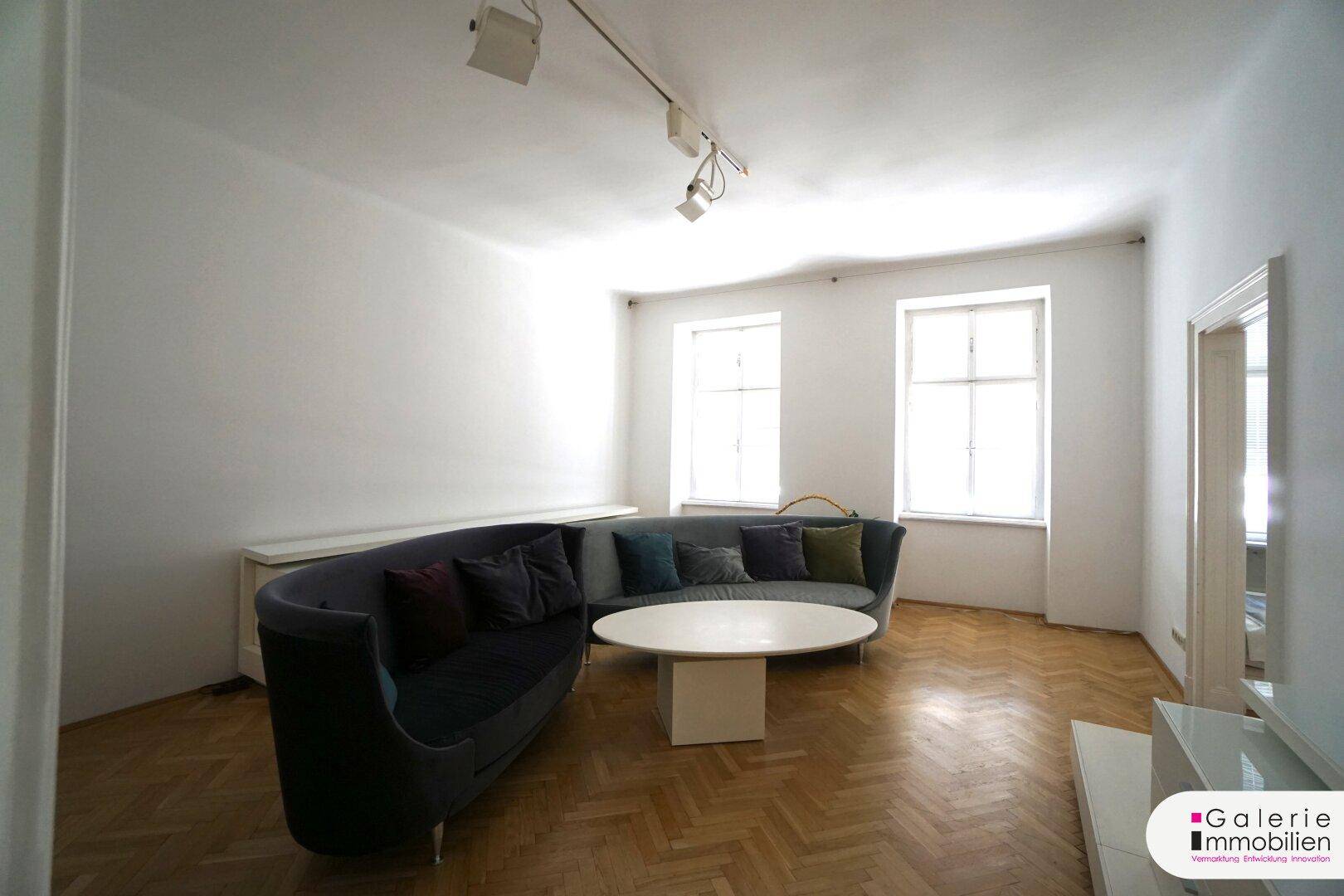 Gemütliches Wohnzimmer mit geschwungenem Sofa, Couchtisch und hellem Fischgrätparkett.