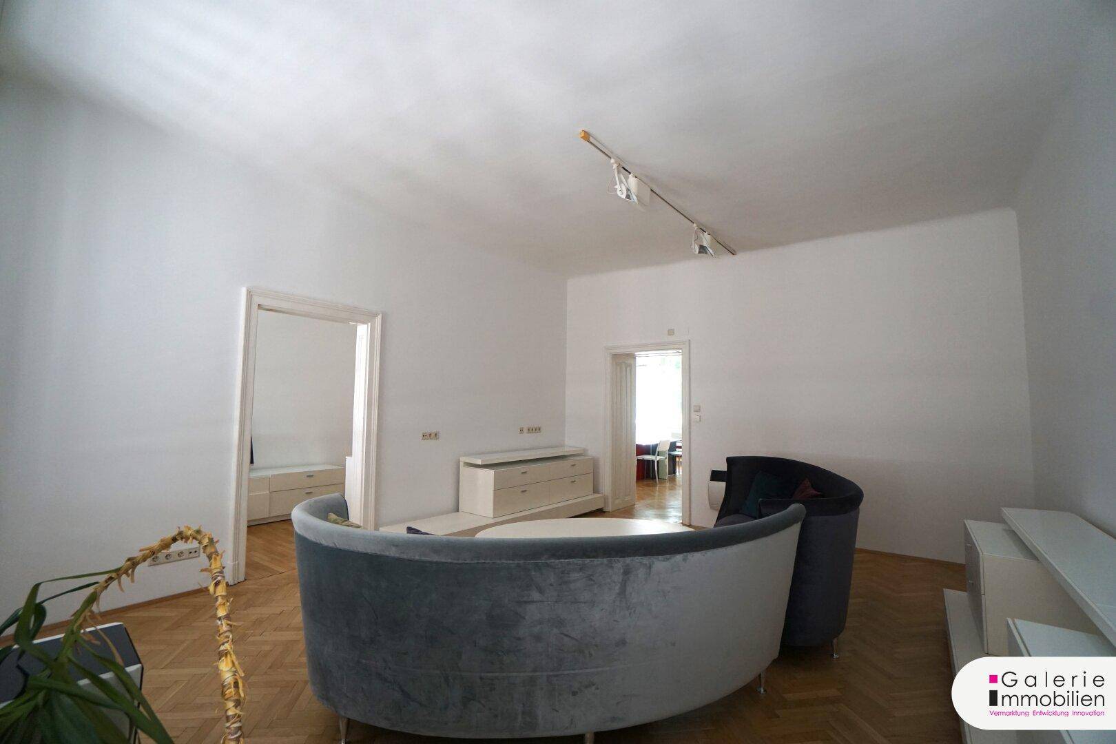 Geräumiges Wohnzimmer mit stilvoller, geschwungener Couch und hellem Ambiente.