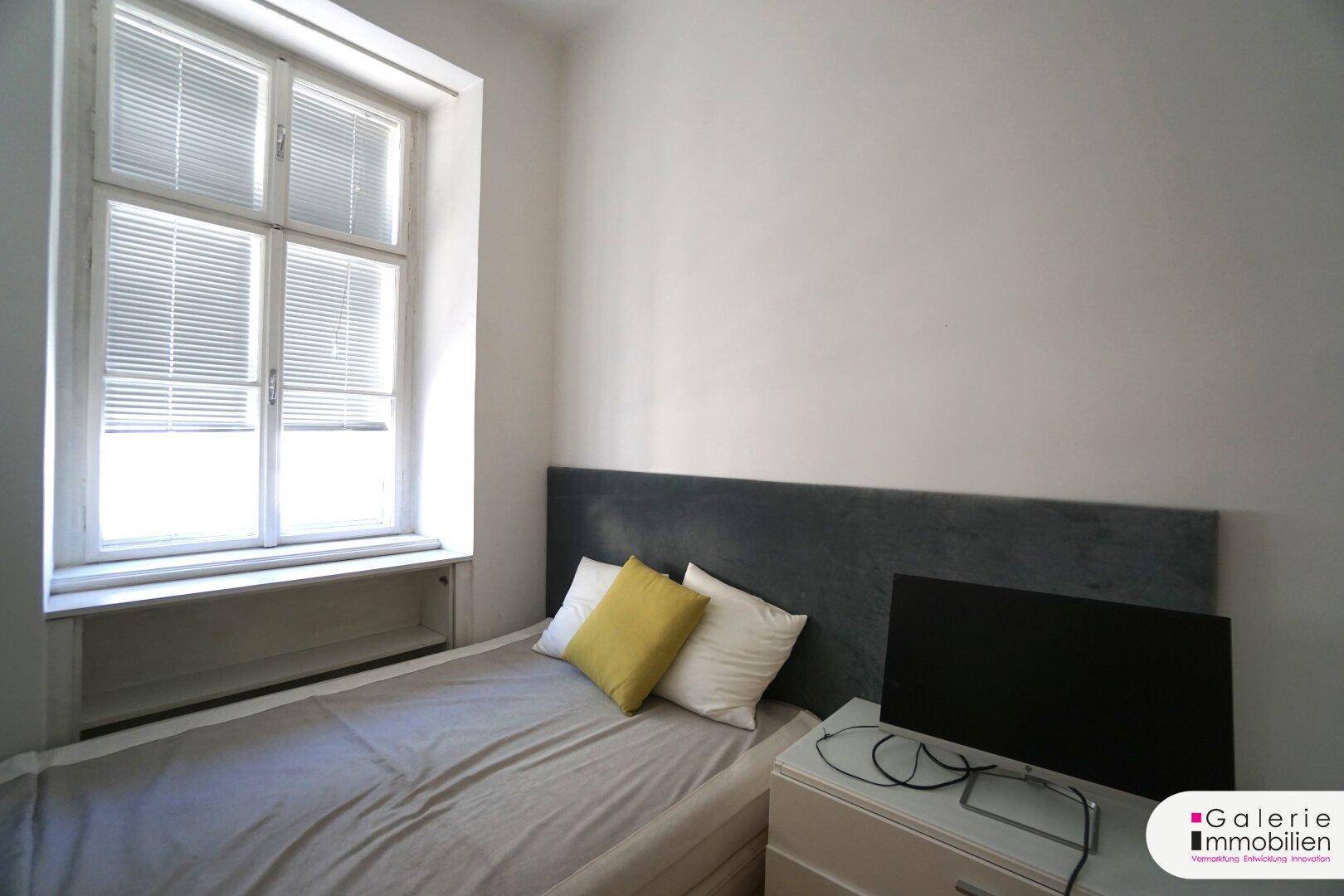 Gemütliches Schlafzimmer mit Einzelbett, modernem Kopfteil und Fenster mit Jalousien.