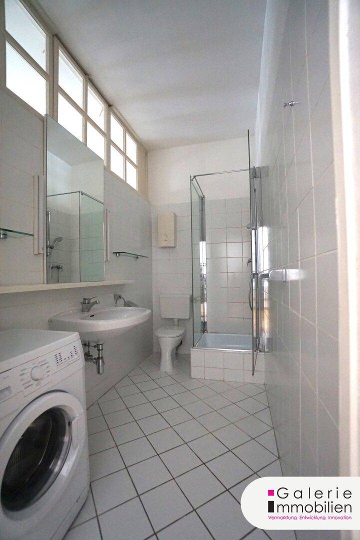Modernes Badezimmer mit weißen Fliesen, Dusche, Waschbecken und Waschmaschine.