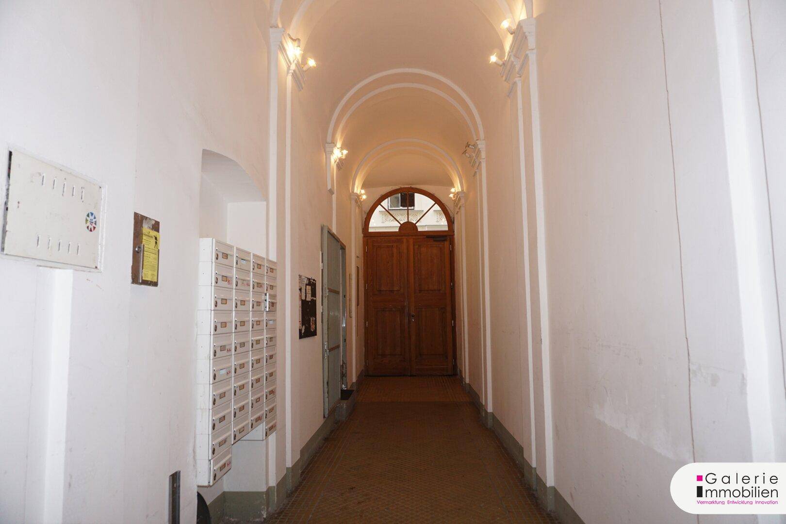 Langer Eingangsbereich mit gewölbter Decke, Briefkästen und einer Holztür am Ende.