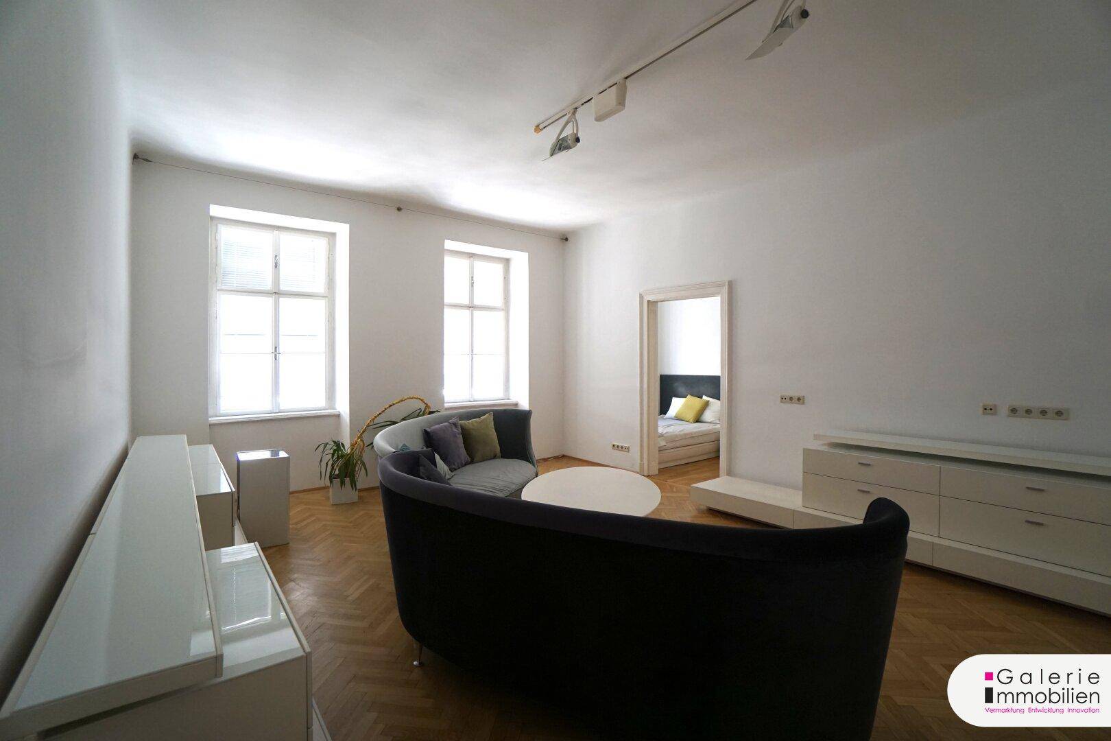 Helles Wohnzimmer mit bequemer Couch und Zugang zu einem weiteren Zimmer.