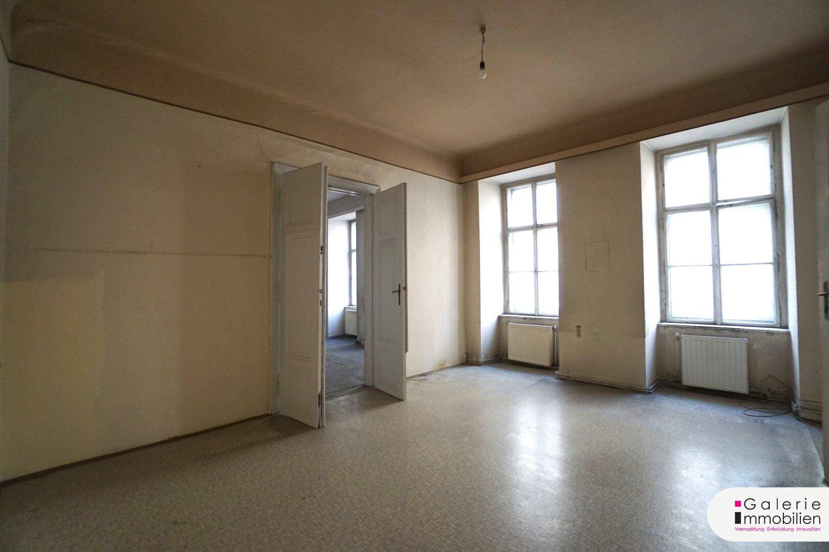 Heller, unmöblierter Raum mit zwei großen Fenstern und Doppeltüren, ideal für eine Neugestaltung.