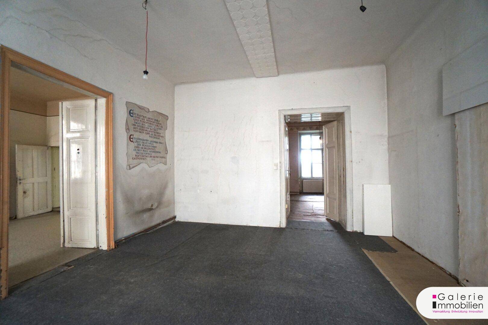 Leerer Raum mit dunklem Teppichboden und zwei Türen, der auf eine umfassende Renovierung wartet.