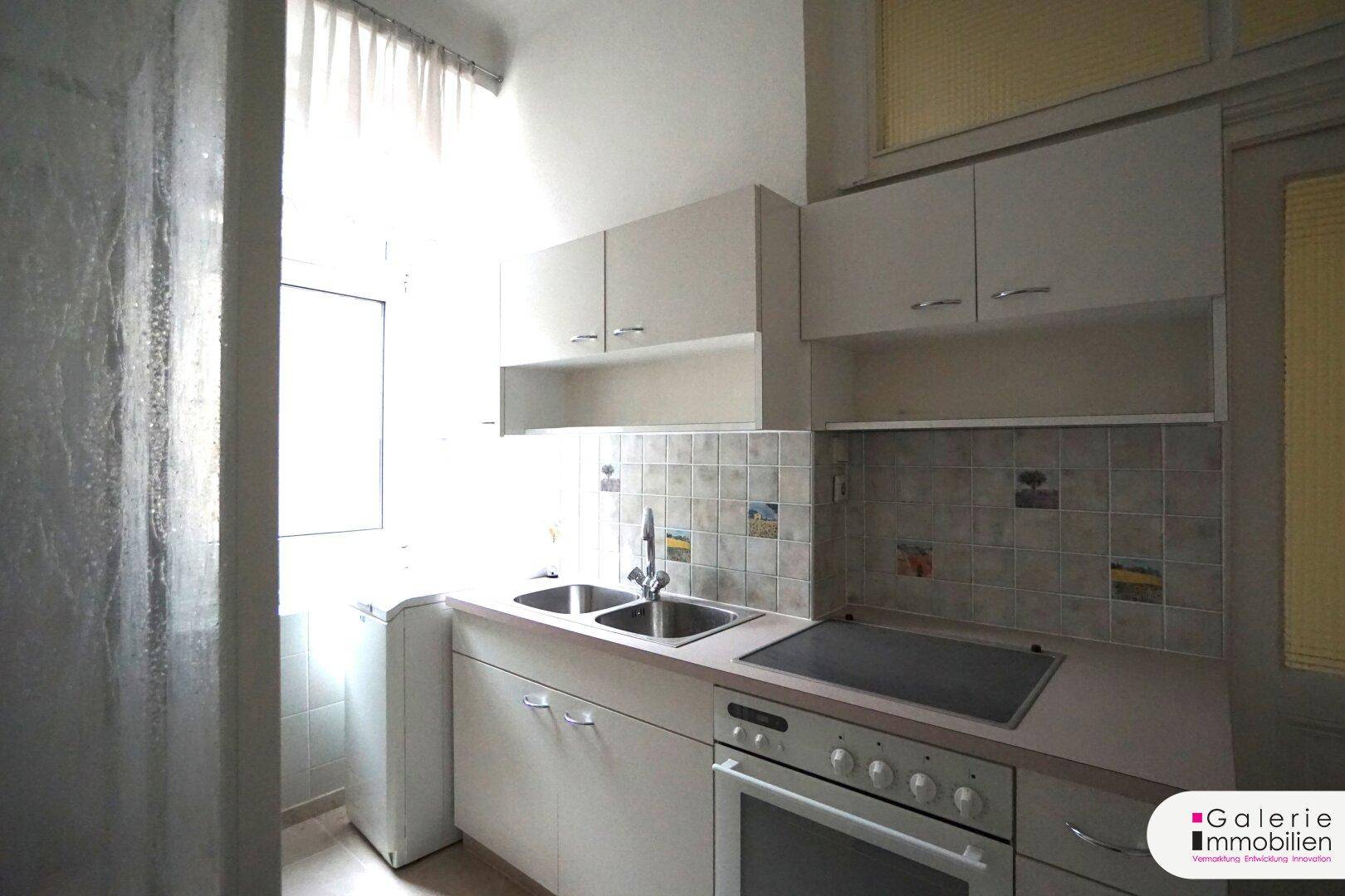 Kleine Küchenzeile mit Spüle, Kochfeld und Oberschränken, ideal für eine Singlewohnung.