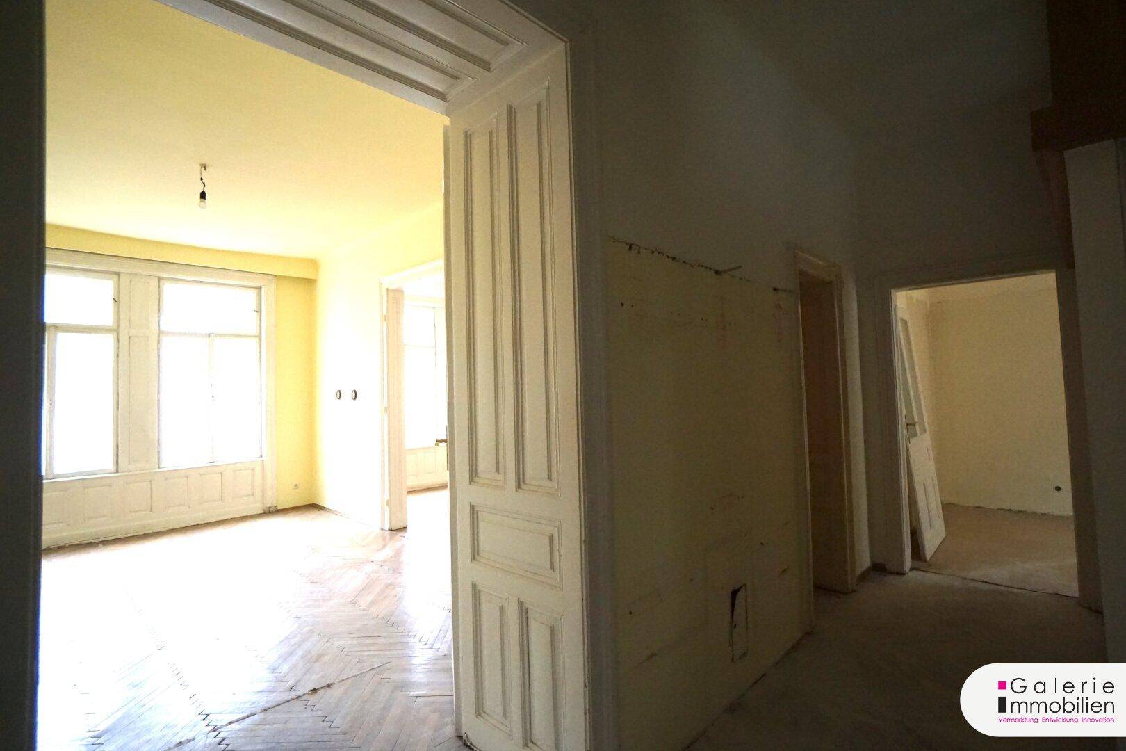 Blick vom Flur durch eine hohe Tür in ein Zimmer mit Fischgrätparkett.