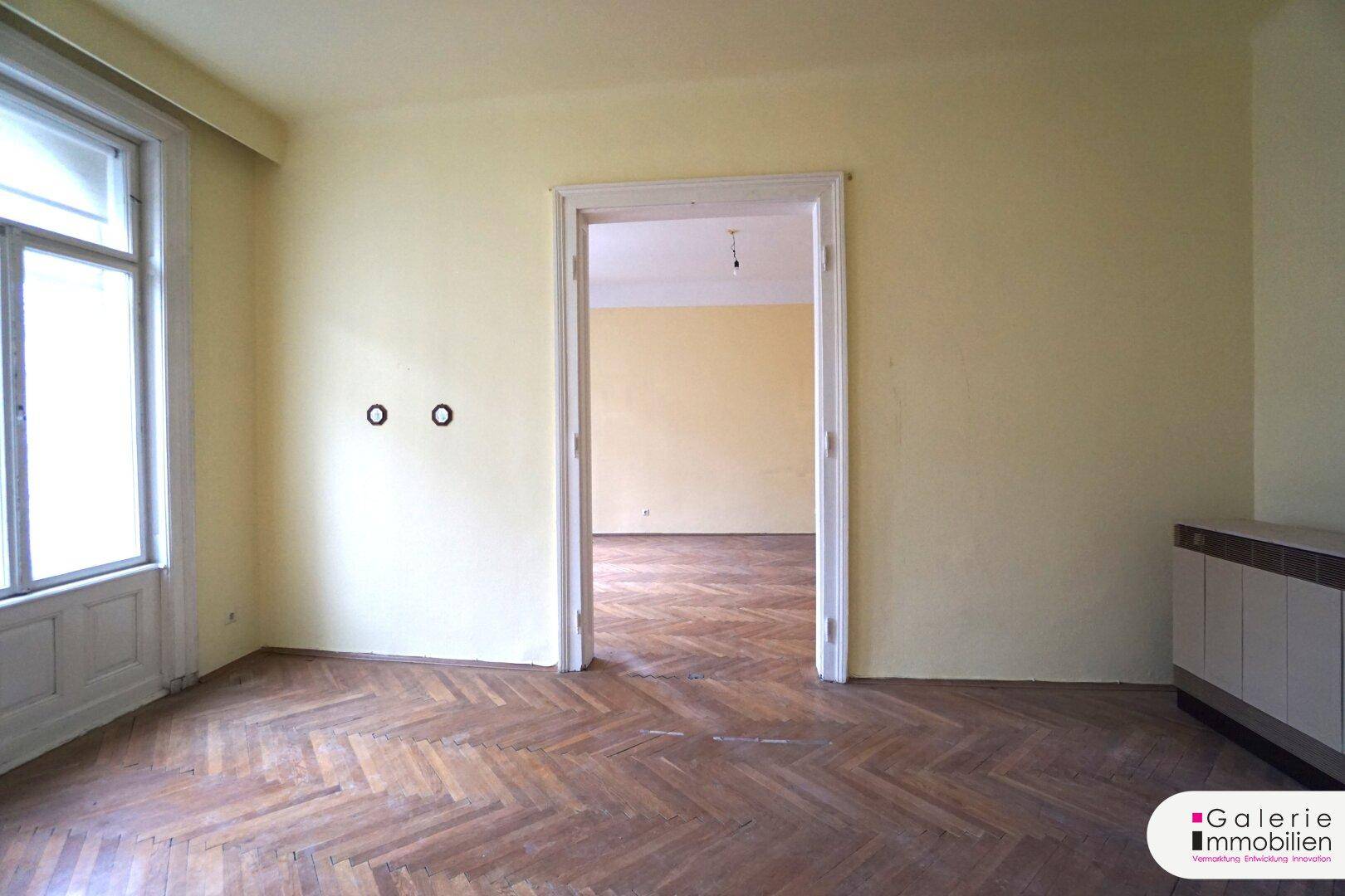 Helles Zimmer mit Fischgrätparkett, Fenster und vorbereiteten Wandanschlüssen.