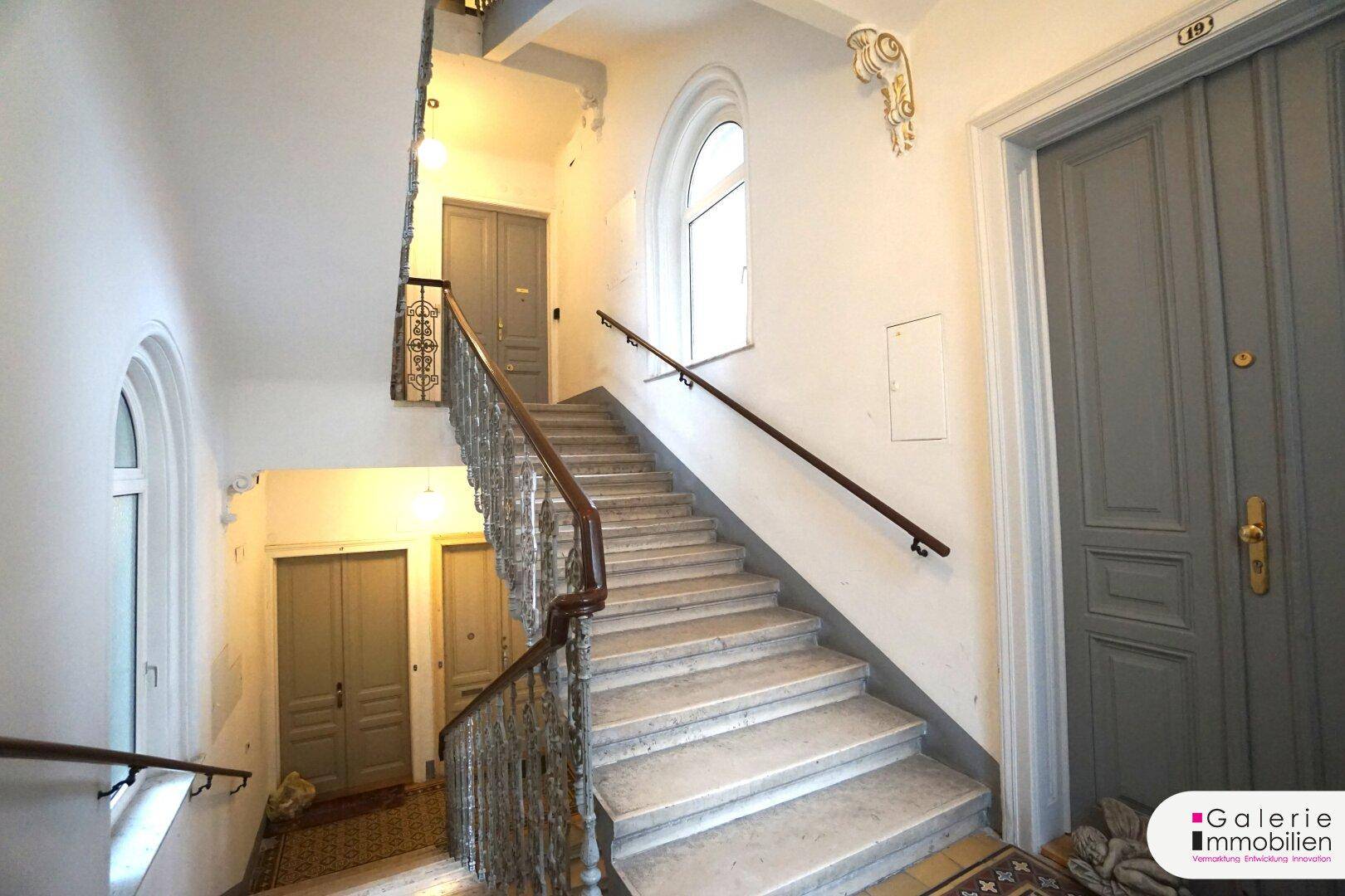 Weitläufiges Treppenhaus in einem Altbau mit mehreren Etagen und großen Fenstern.