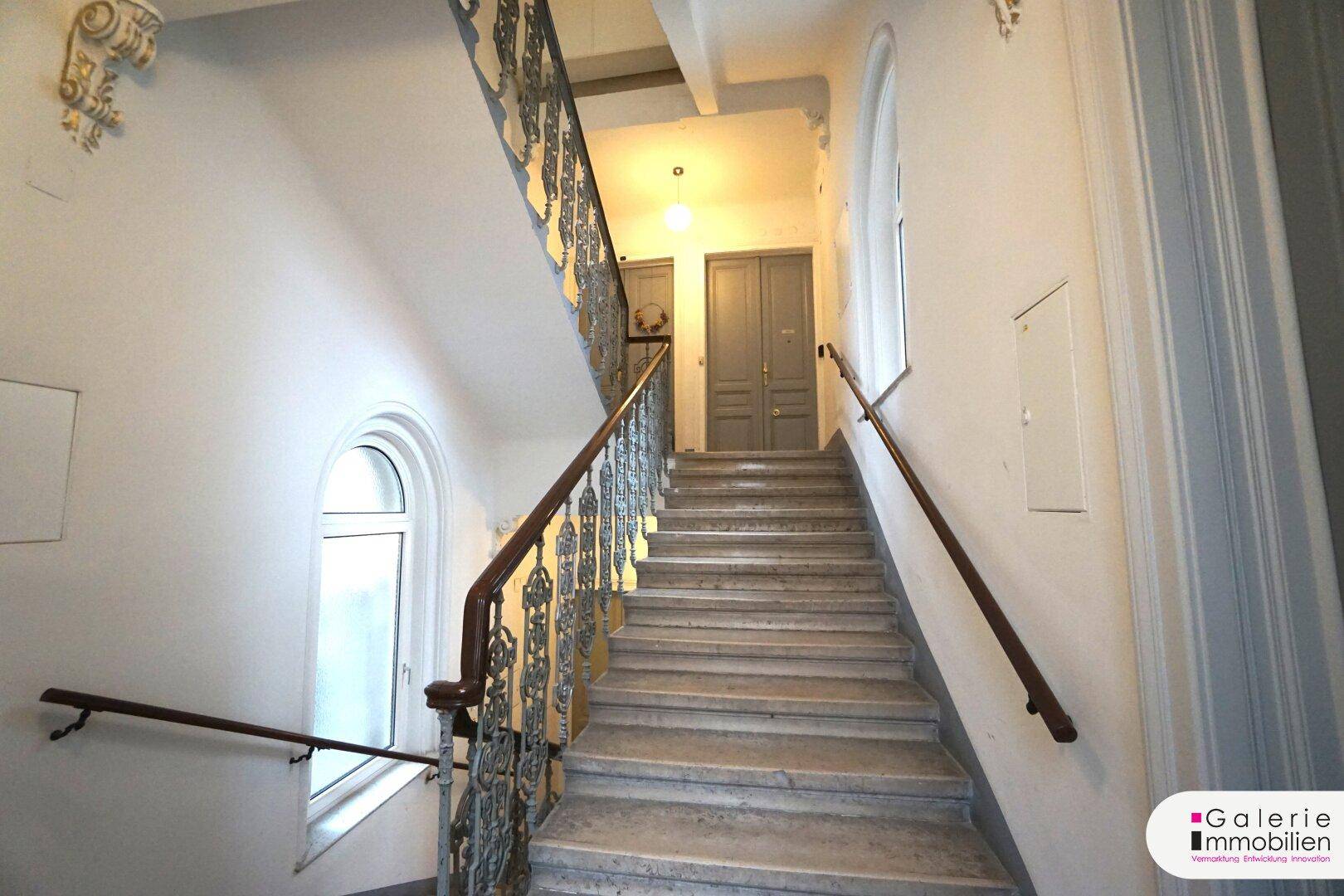 Helles Treppenhaus in einem Altbau mit geschwungenem Geländer und Tageslicht.
