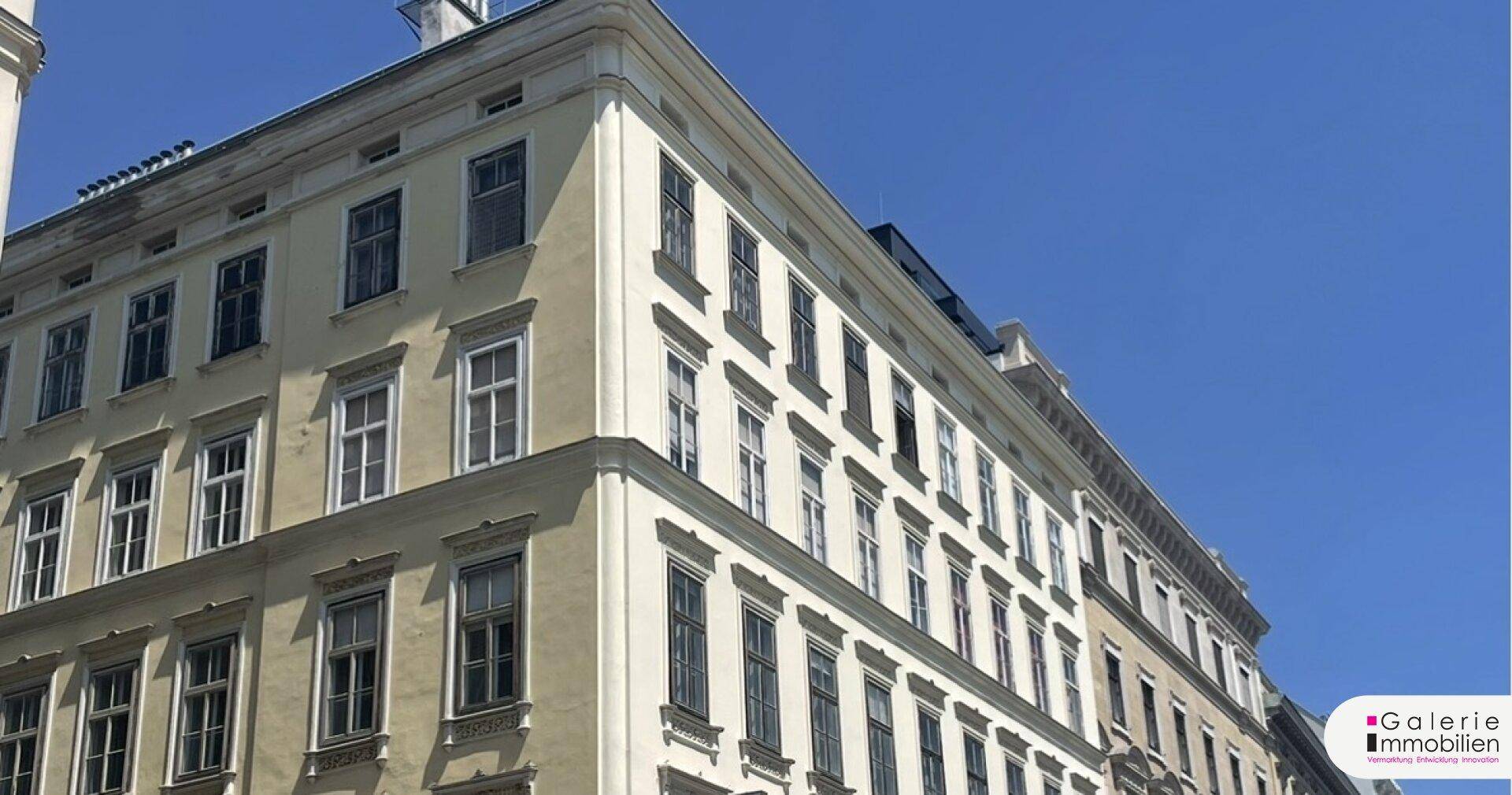 Historische Fassade eines Mehrfamilienhauses mit vielen Fenstern unter blauem Himmel.