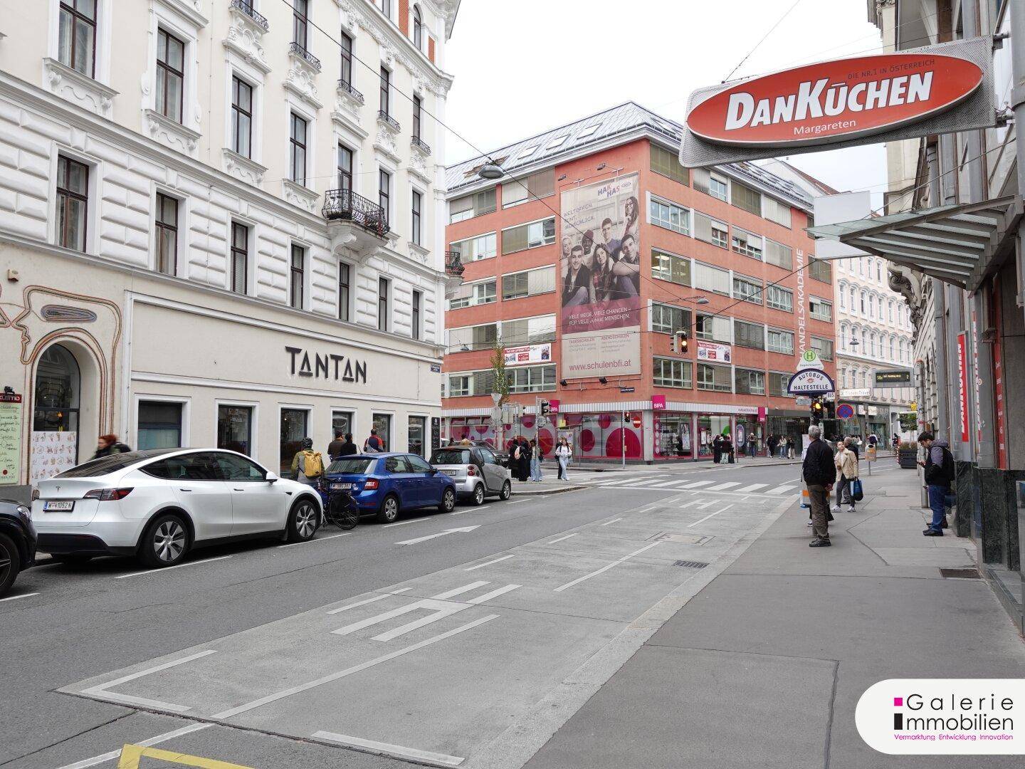 Blick auf die belebte Stadtstraße mit umliegenden Gebäuden und parkenden Autos.