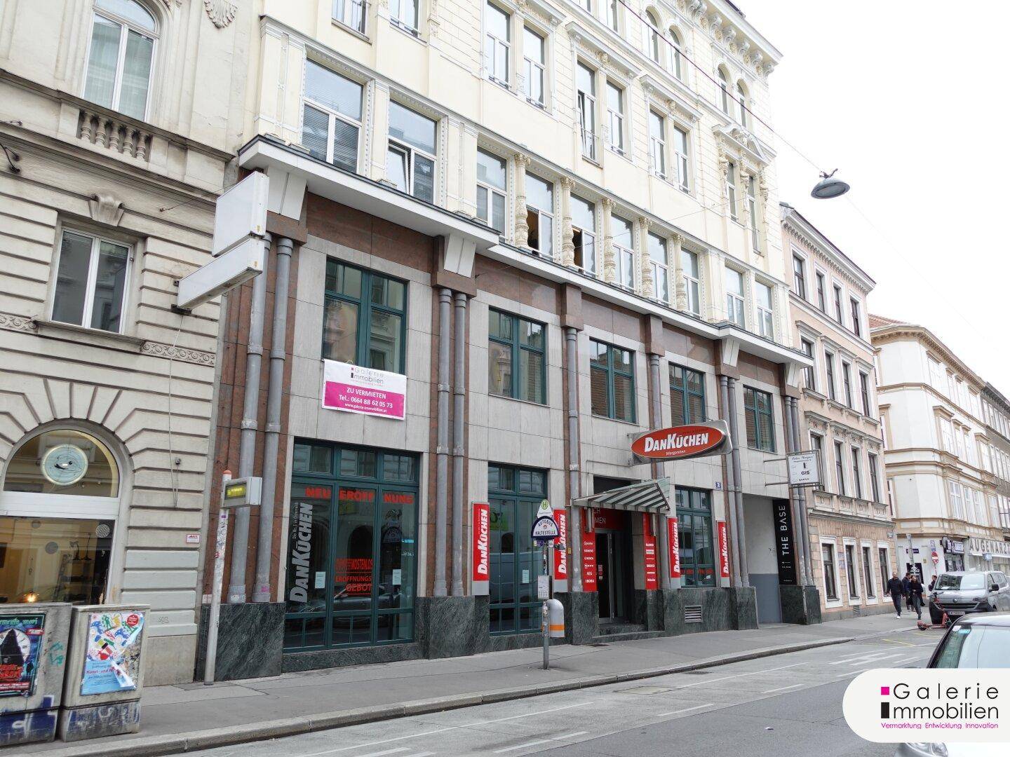 Seitenansicht des Gebäudes mit Geschäften im Erdgeschoss und belebter Straße.