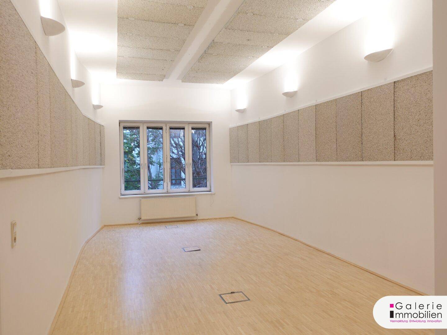 Heller Raum mit Holzboden, großen Fenstern und schallabsorbierenden Decken- und Wandpaneelen.