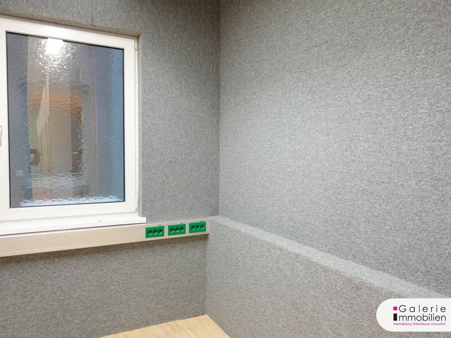 Kleiner Raum mit Fenster und grauer, strukturierter Wandverkleidung.