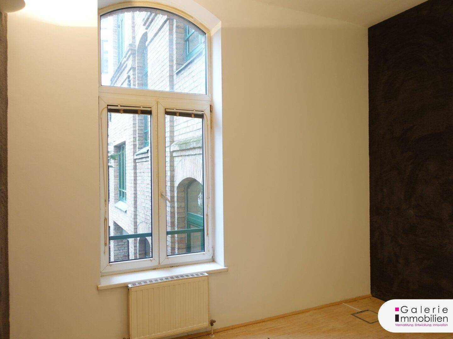Heller Raum mit einem hohen Bogenfenster und Holzboden.
