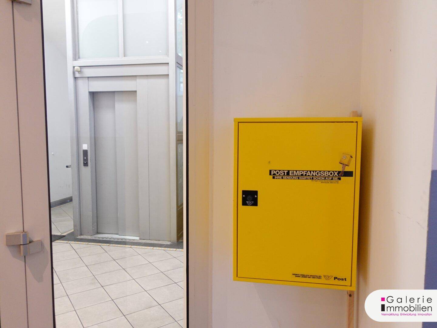 Moderner Aufzug und gelber Briefkasten im Eingangsbereich des Gebäudes.