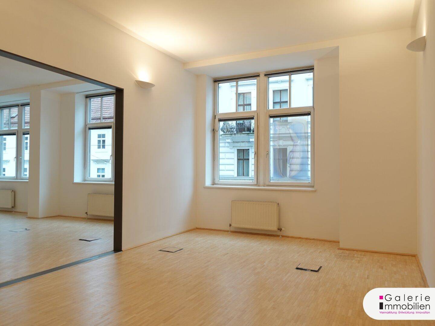 Heller Raum mit großen Fenstern, die viel Tageslicht hereinlassen, und Holzboden.