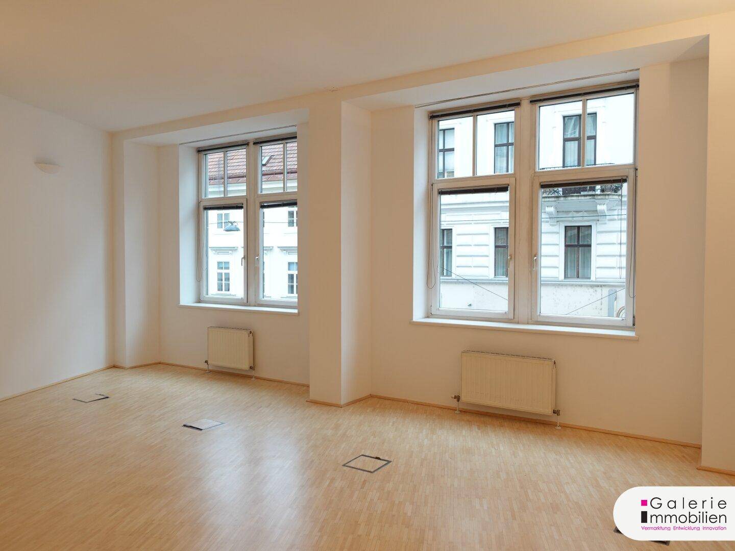 Geräumiger, heller Raum mit zwei großen Fenstern und hellem Holzboden.