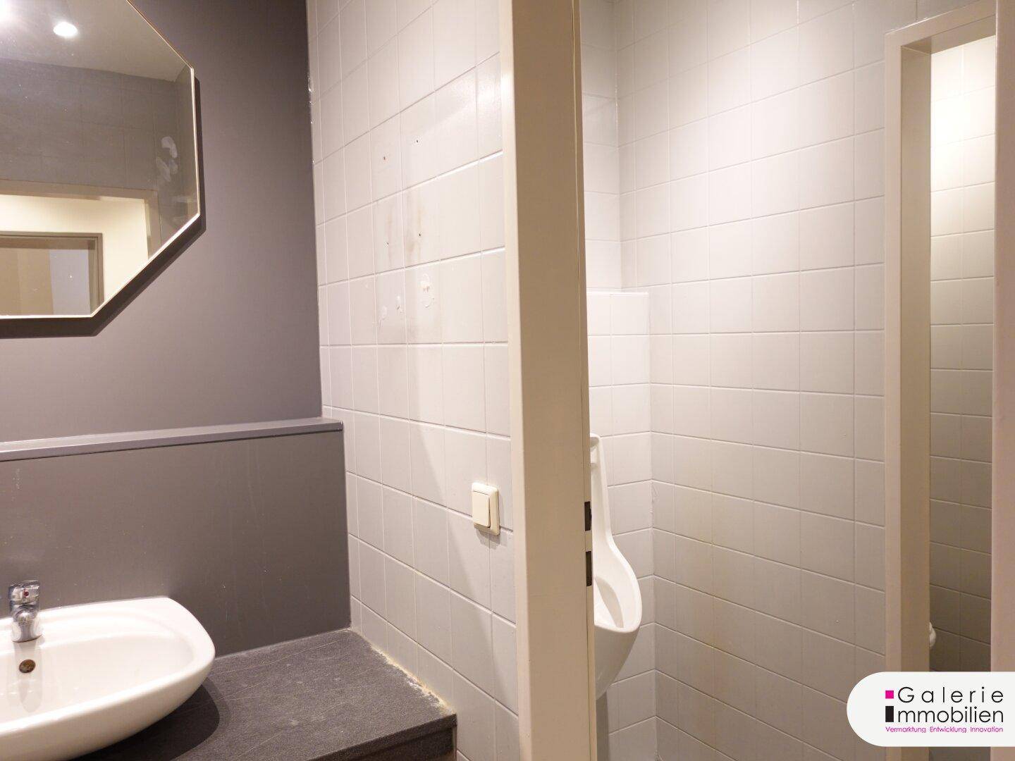 Modernes Gäste-WC mit Urinal, Waschbecken und hellen Fliesen.